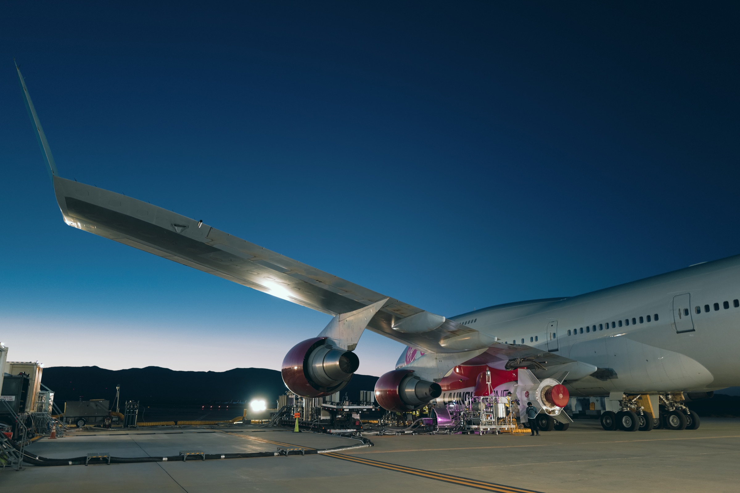 Cosmic Girl aircraft with LauncherOne beneath the wing during twilight ground operations.